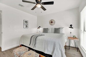 Ein Schlafzimmer mit einem Bett, einem Deckenventilator, einem Nachttisch mit Lampe und einer Wanduhr.