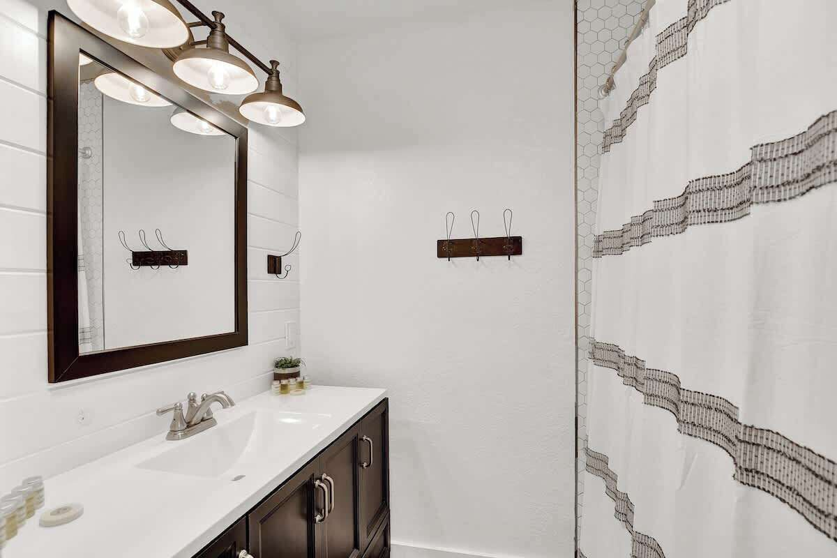 A bathroom with a white sink, dark cabinets, and a mirror with three lights.