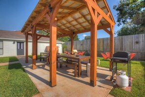 Eine Holzpergola mit Tisch, Stühlen, einem Grill und einem Propangasbehälter.