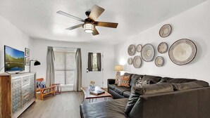 Una sala de estar moderna con un sofá de cuero, un mueble de madera, un ventilador de techo y placas decorativas en la pared.
