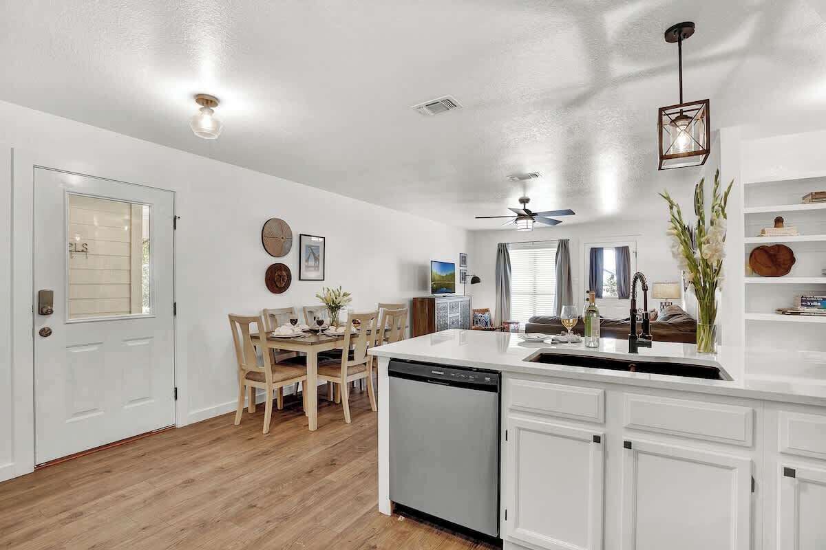 A modern kitchen with white cabinetry, a dishwasher, and a dining area with wooden chairs and a table.