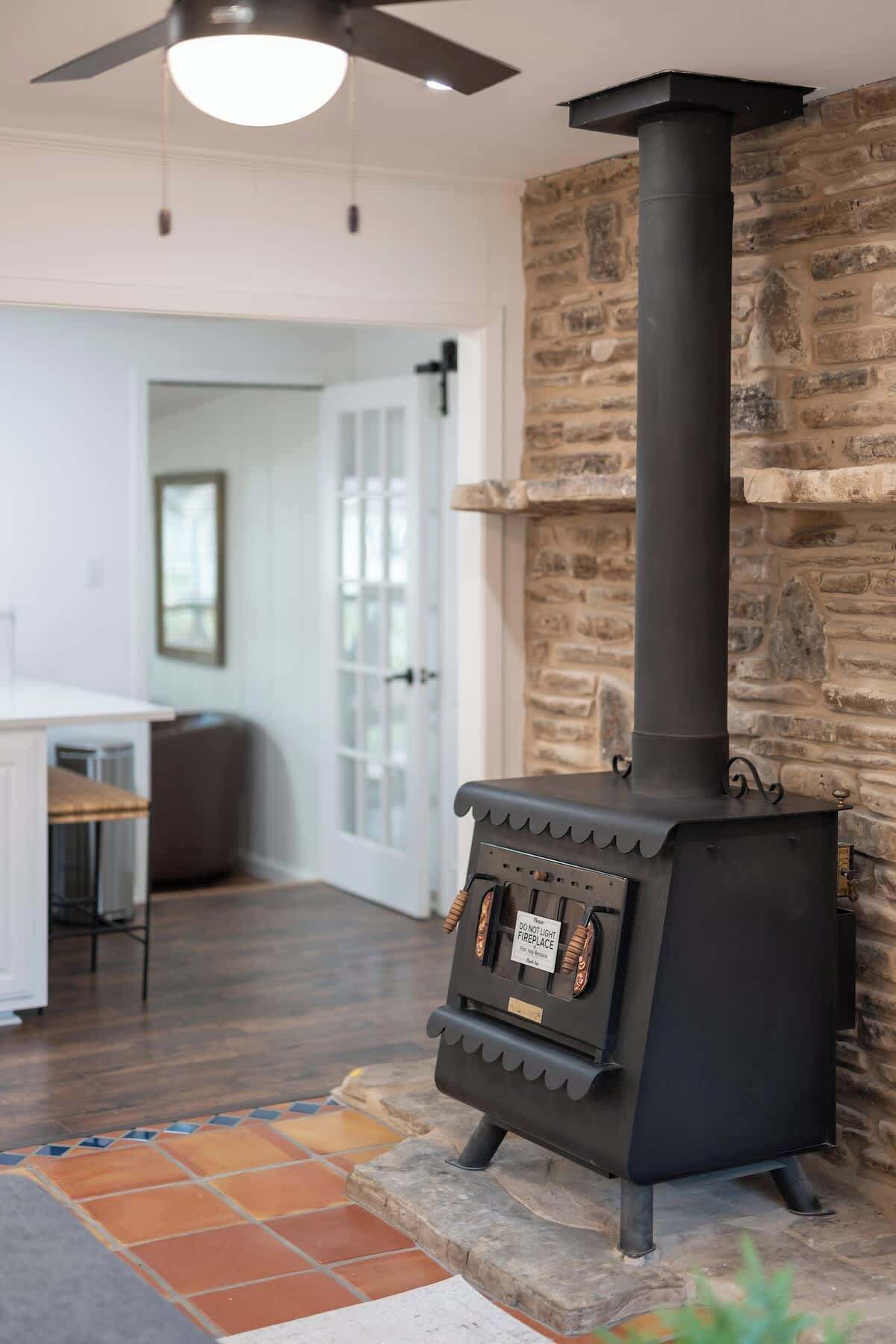 A modern kitchen with a built-in wood stove, stone wall, and a dining area with a view of the outdoors.