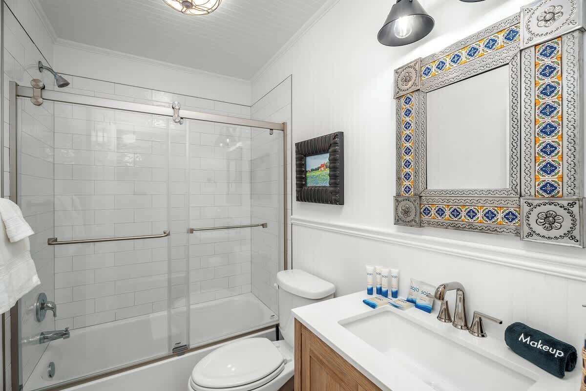 A bathroom with a glass shower enclosure, a toilet, a sink with toiletries, and a decorative mirror.