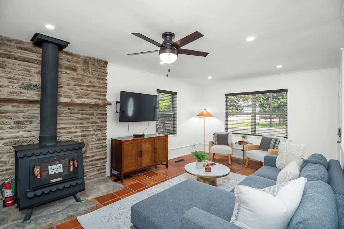 A living room with a stone wall, a black wood-burning stove, a ceiling fan, a TV, a sofa, and a lamp.