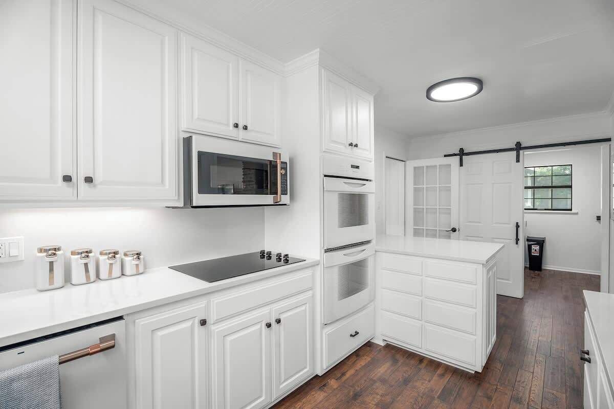 Une cuisine moderne avec des meubles blancs, des appareils électroménagers en acier inoxydable et un plancher en bois.