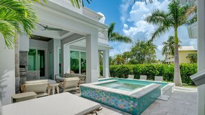 Un área de piscina moderna al aire libre con sillones reclinables, un jacuzzi y un solárium con baldosas.