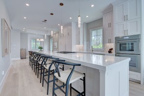 Una cocina moderna con armarios blancos, una isla alargada con taburetes altos y electrodomésticos de acero inoxidable.