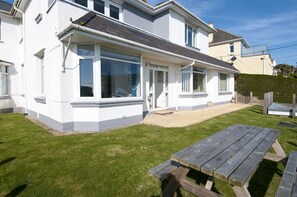 A two-story house with a large front window, a patio area, and a wooden picnic table.