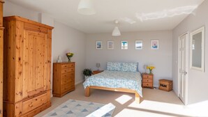 Ein Schlafzimmer mit einem Holzschrank, einem Bett mit gemusterten Betttextilien, einem kleinen Nachttisch und einer Wand mit gerahmten Bildern.