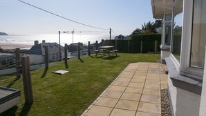 Eine Terrasse mit Meerblick, eine Rasenfläche und ein Gebäude mit einem Fenster.