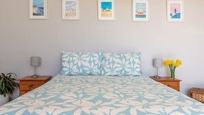 Ein Schlafzimmer mit einem Bett, zwei Nachttischen, einer Lampe, einer Pflanze und einer Wand mit fünf gerahmten Bildern.
