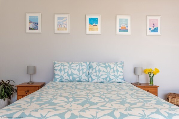 A bedroom with a bed, two nightstands, a lamp, a plant, and a wall with five framed pictures.