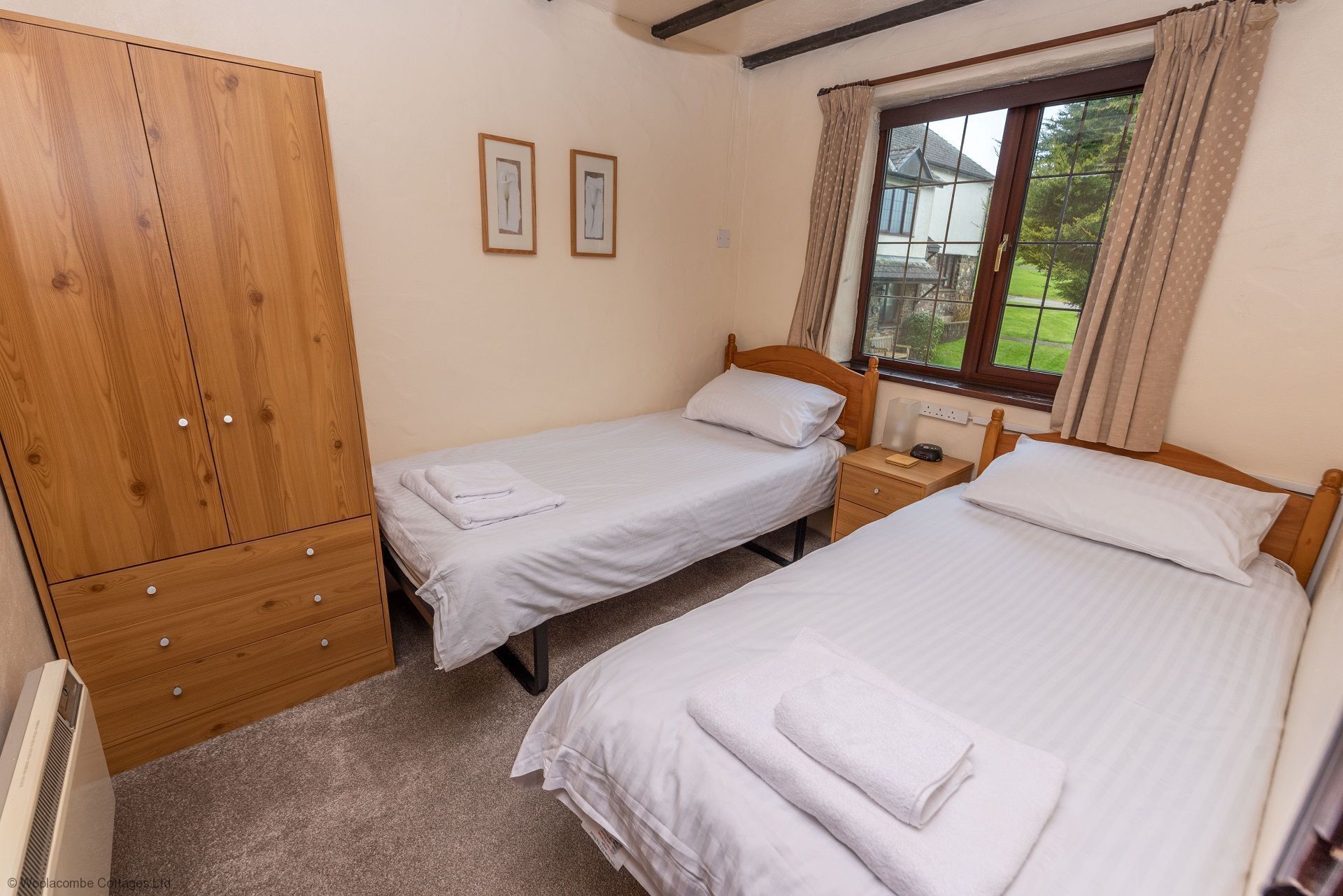 Un dormitorio con dos camas individuales, un armario de madera y una ventana con cortinas.