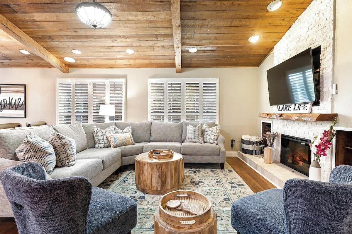 A cozy living room with a wooden ceiling, a fireplace, and a large TV mounted on the wall.