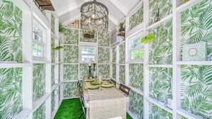 A room with a green artificial grass floor, white walls with a leaf pattern, a dining table set with a green table runner, and a hanging light fixture. - Charming Cottage Near Main With Patio&firepit!! (Fredericksburg)