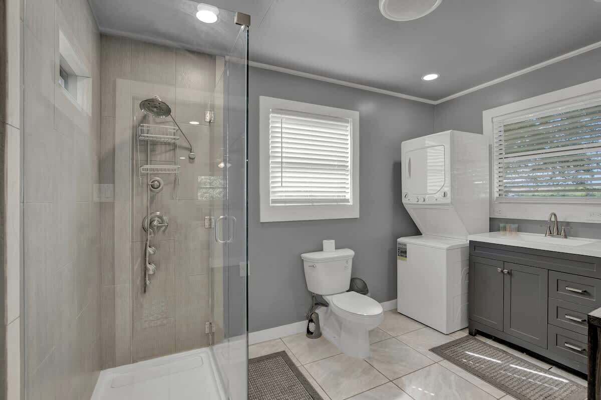 Une salle de bain moderne avec une douche à parois de verre, des toilettes, un meuble-lavabo avec un miroir et une fenêtre avec des stores.