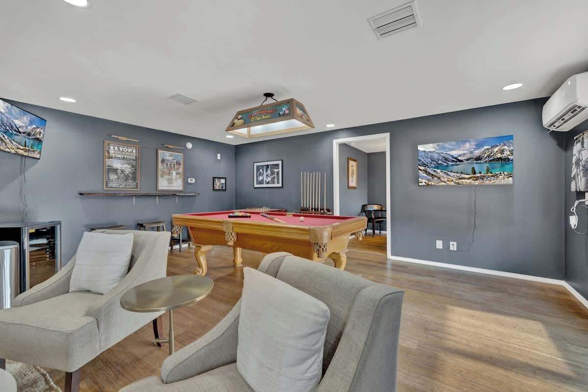 A modern living room with a pool table, comfortable seating, and artwork on the walls.