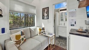 A modern interior with a sofa, a small table, a kitchen area, and a view of the outdoors.