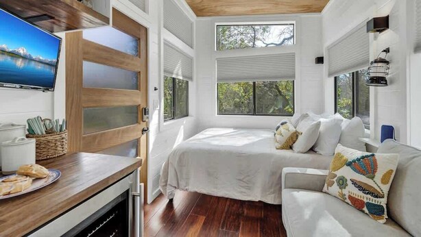 A bedroom with a bed, a TV, a wooden desk, and a window with blinds.