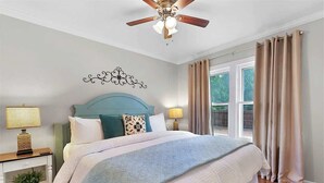 A bedroom with a bed, nightstands, a ceiling fan, and a window with curtains. - New! Charming Home Just 4 Blks From Main St! (Fredericksburg)