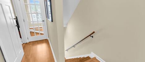 A hallway with a wooden floor, a white door, and a staircase with a handrail.