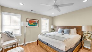 Un dormitorio con cama, dos lámparas de noche, ventilador de techo y una ventana con persianas.