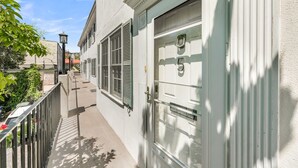 Un estrecho callejón con un edificio blanco que cuenta con una puerta grande, ventanas, una pequeña escalera y una valla de metal.