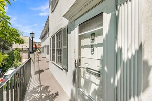 A narrow alleyway with a white building featuring a large door and windows, a small staircase, and a metal fence. - Dreamy Downtown Condo, Near Meeting St & Broad St (Charleston)
