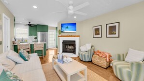 Una sala de estar con chimenea, televisor y comedor con armarios verdes.