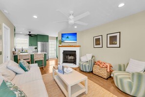 A living room with a fireplace, a television, and a dining area with green cabinets. - Dreamy Downtown Condo, Near Meeting St & Broad St (Charleston)