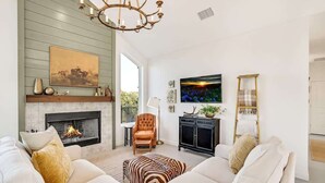 Una sala de estar con chimenea, un conjunto de sofás, una araña y un televisor.