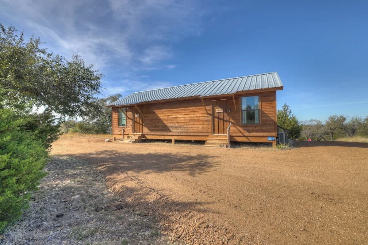 A wooden cabin with a metal roof, situated in a dry, open landscape with sparse vegetation.