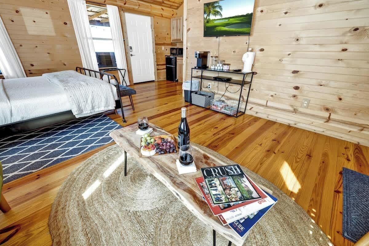 A cozy wooden cabin with a bed, a dining table with a magazine, a TV, and a kitchen area.