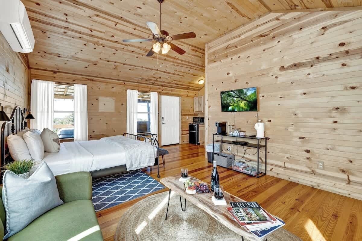Interior acogedor de una cabaña de madera con cama, sofá, mesa de comedor y televisor.