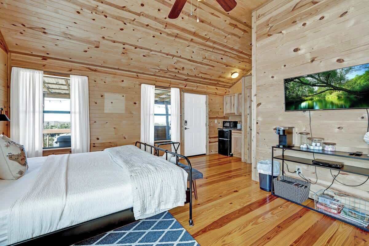 Un dormitorio de cabaña de madera con cama, escritorio, televisión y ventana con cortinas.