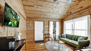 A wooden cabin interior with a TV, sofa, and dining area. - Mesquite Cabin With Hot Tub & Hill Country Views (Fredericksburg)
