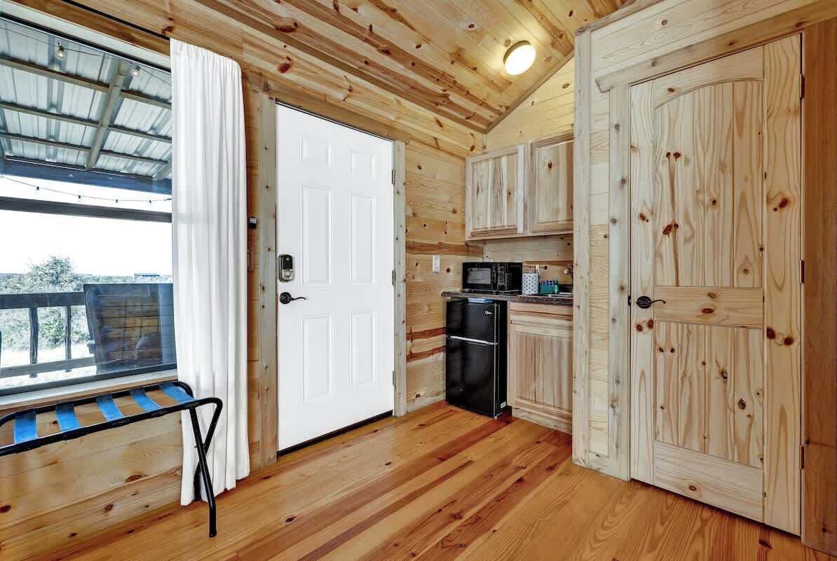 A wooden cabin interior with a kitchen, a door, and a window with curtains.