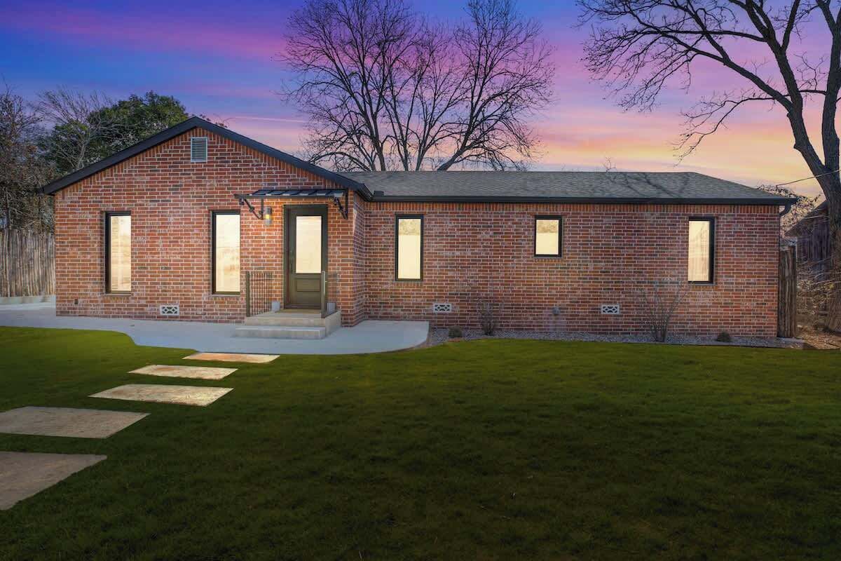 A brick house with a front porch, a garage, and a well-maintained lawn.