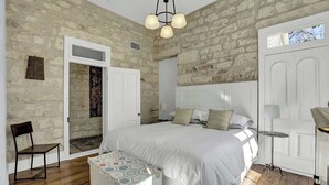A bedroom with a large bed, a chair, a small table, and a hanging light fixture.