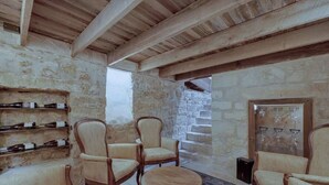 A rustic interior with stone walls, wooden beams, and a stone staircase. There are several upholstered chairs and a small round table.