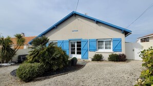 A building with a sloped roof, a beige facade, and blue shutters. There are potted plants and a gravel driveway. - A 5mn de la mer et du Bourg ,une Villa Plain Pied Vous Attend ! (Préfailles)