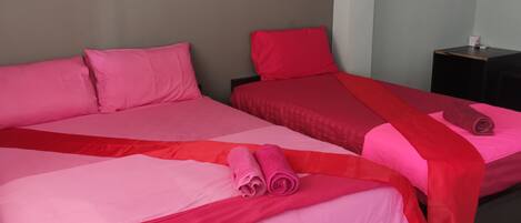 A hotel room with two beds, each with pink bedding and red pillows. There is a framed picture on the wall above the beds.
