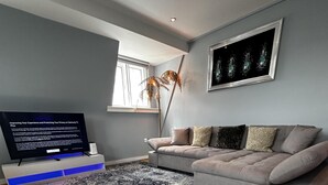 A modern living room with a grey sofa, a patterned rug, a flat-screen TV, and a tall plant. - Immaculate 1-bed Apartment in Chelsea London (London)