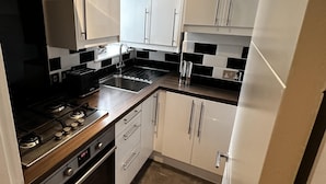 A compact kitchen with white cabinets, a stainless steel stove, and a black and white tiled backsplash. - Immaculate 1-bed Apartment in Chelsea London (London)