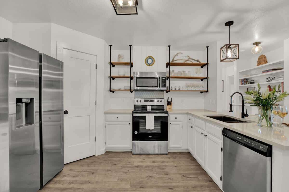 Une cuisine moderne dotée d’appareils électroménagers en acier inoxydable, de meubles blancs et d’un plancher en bois.