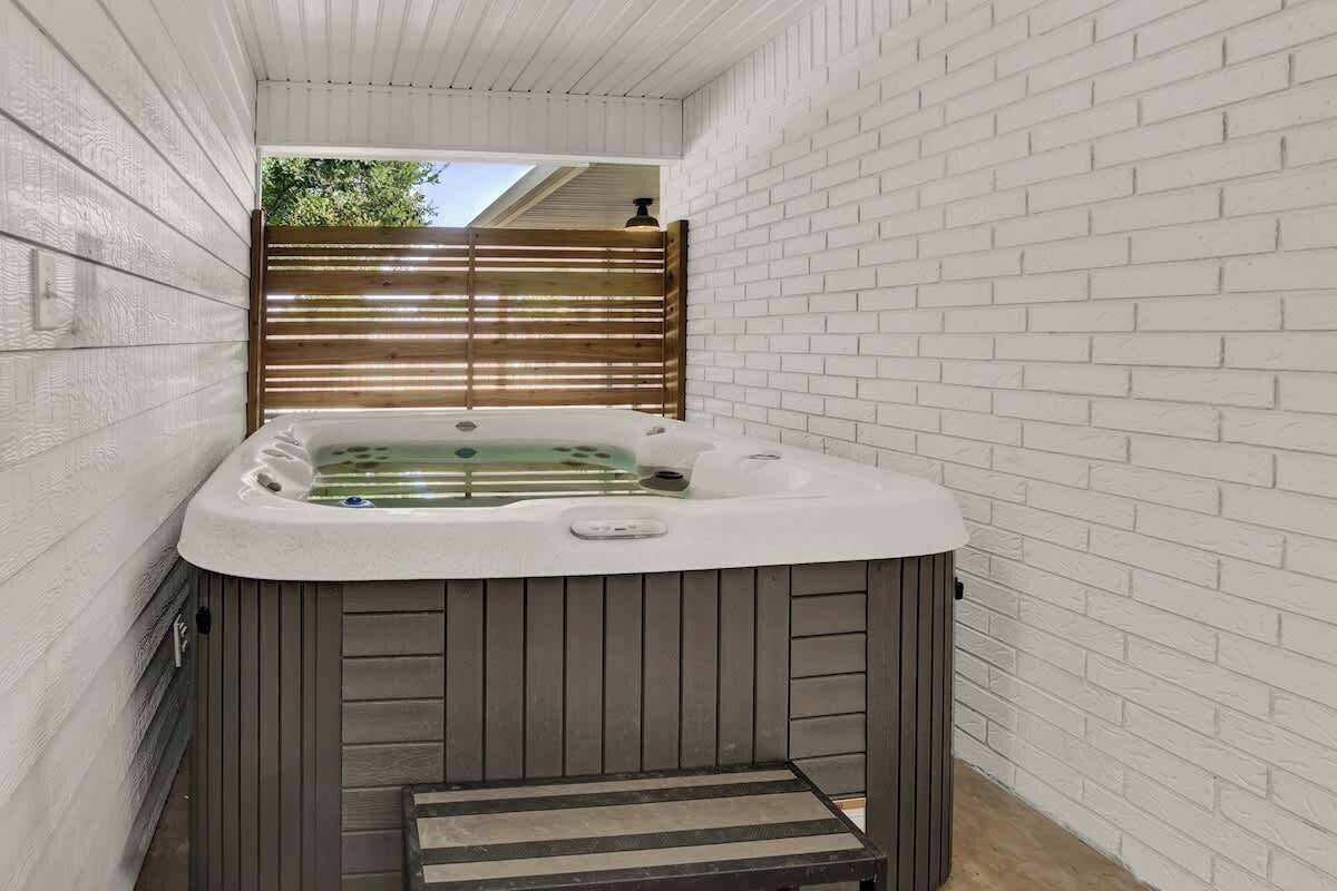 A hot tub in a narrow space with white brick walls and a wooden fence.