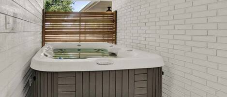 A hot tub in a narrow space with white brick walls and a wooden fence.