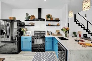 A modern kitchen with a stainless steel refrigerator, black stove, blue cabinets, and a marble countertop. - Luxury Modern Home With Hot tub Deck & Firepit! (Fredericksburg)