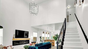 Amplia sala de estar con un televisor de pantalla plana grande, un sofá azul y una escalera con peldaños estampados.