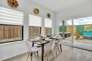A dining area with a table set for four, large windows, and a view of the backyard. - Luxury Modern Home With Hot tub Deck & Firepit! (Fredericksburg)